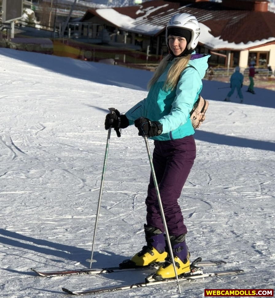 Blonde Girl skiing in Purple Ski Suit and Green Anorak on Webcamdolls